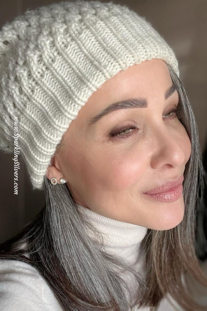 A woman growing out her gray hair with a white beanie