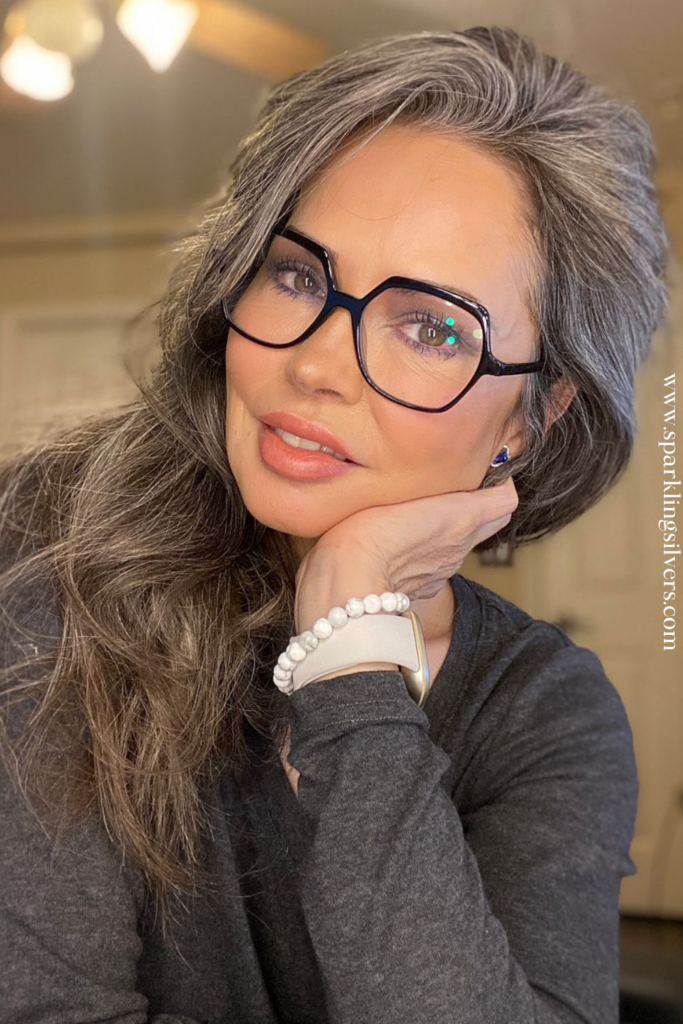 A woman with long grey hair and black glasses