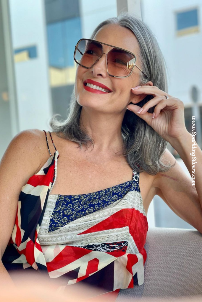 A Woman with gray hair wearing a sun glass and an abstract design dress.